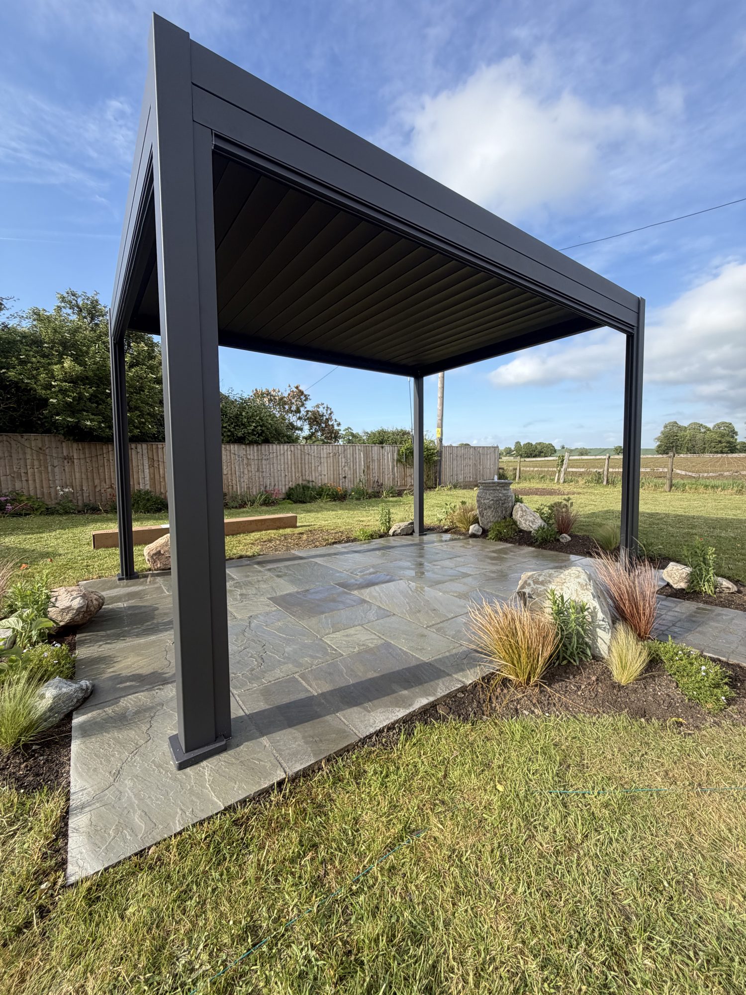 Anthracite aluminium louvred pergola on a riven sandstone patio in a rural garden