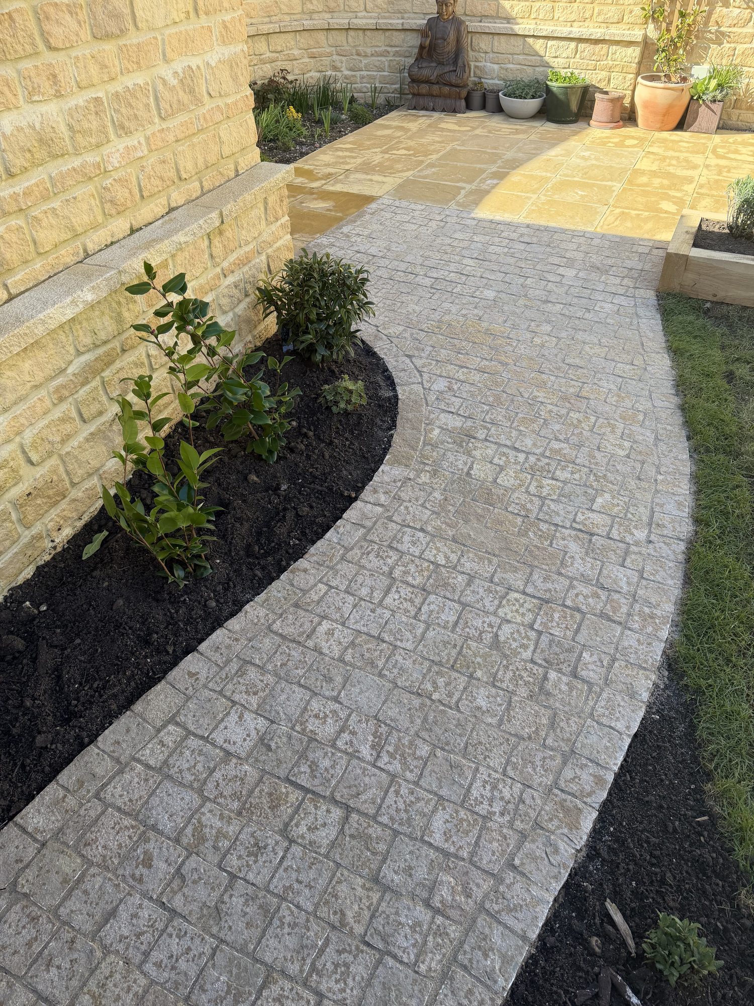 Cobble-effect imprinted concrete path curving past a Cotswold-stone wall