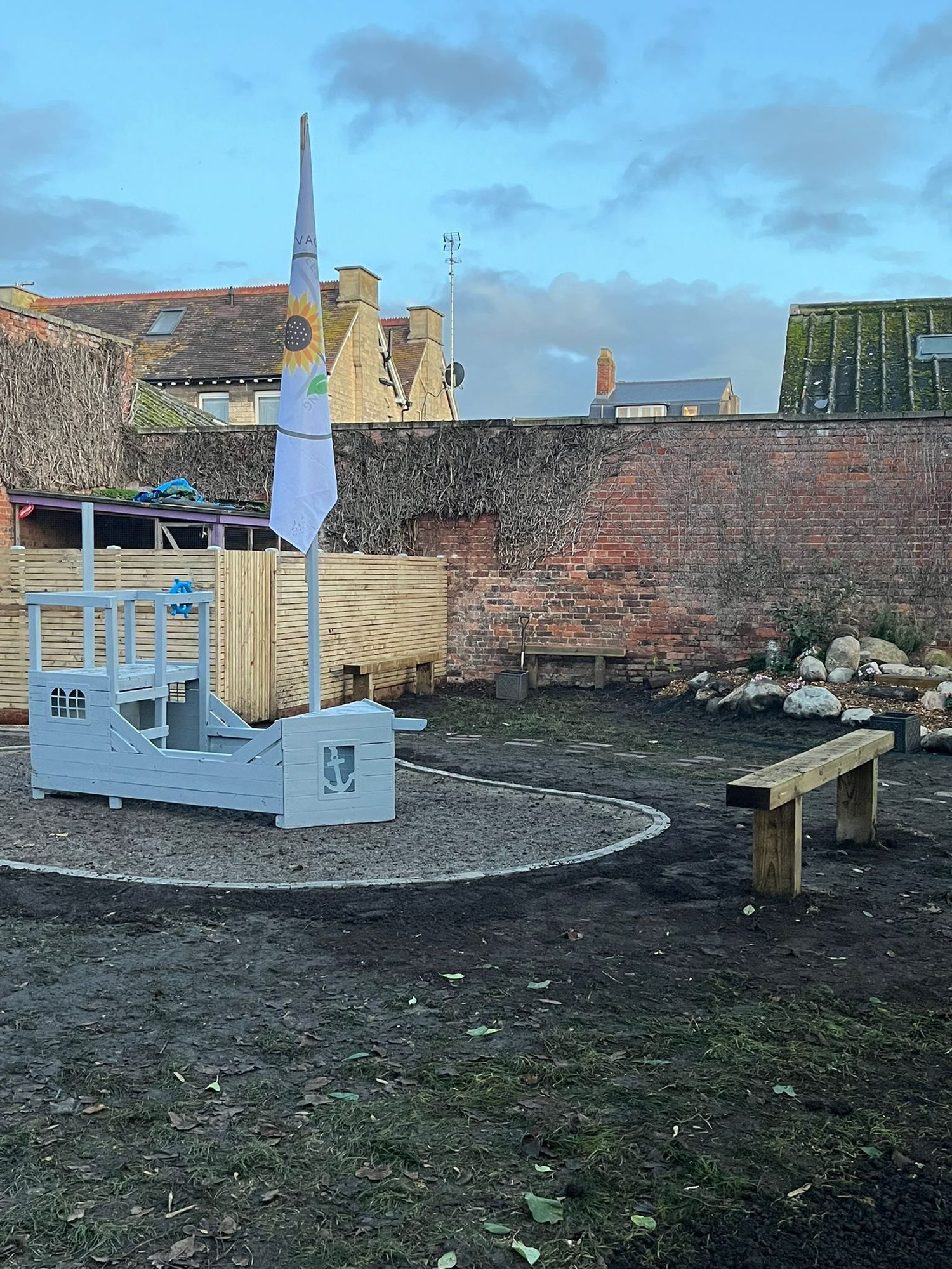 Wooden play boat with a sail mast on a sand pit in the walled play garden