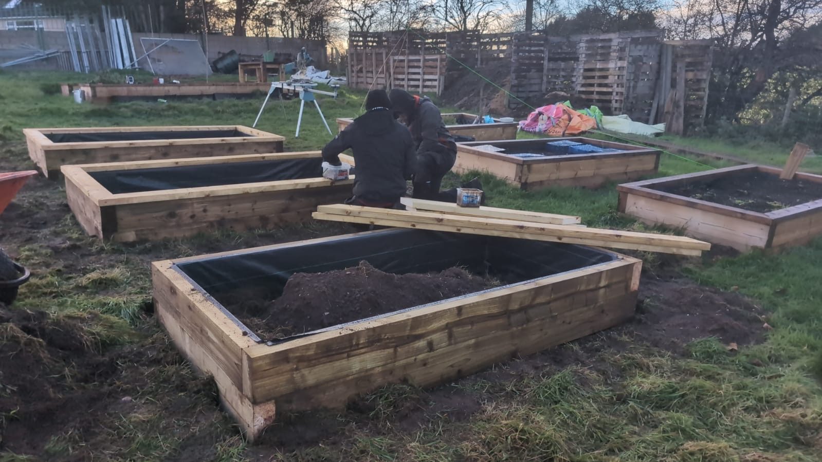 Oak sleeper raised beds being built and filled at dusk during the play garden build