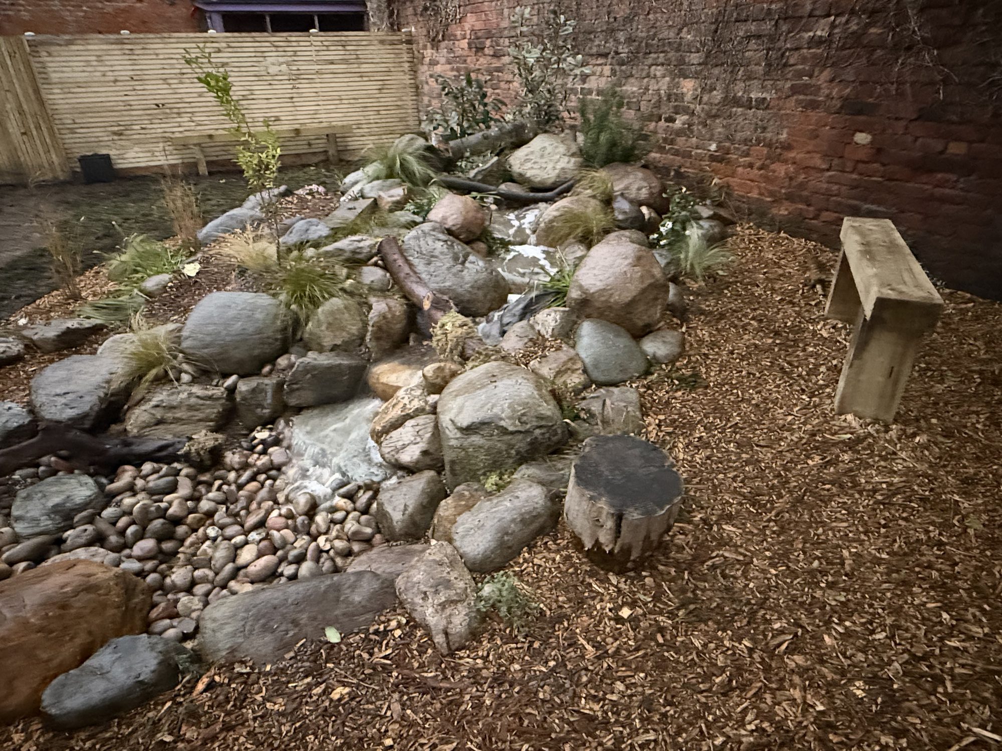 Boulder rockery water feature with bark mulch and a sleeper bench in the play garden