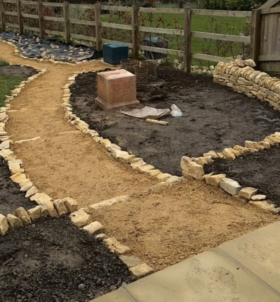 Curved Cotswold dry-stone walled beds and self-binding gravel paths under construction in a rural garden
