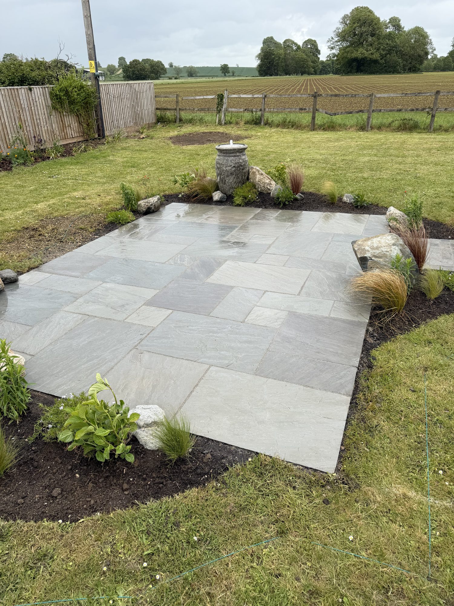 Riven sandstone patio with a stone urn water feature and a ploughed field beyond