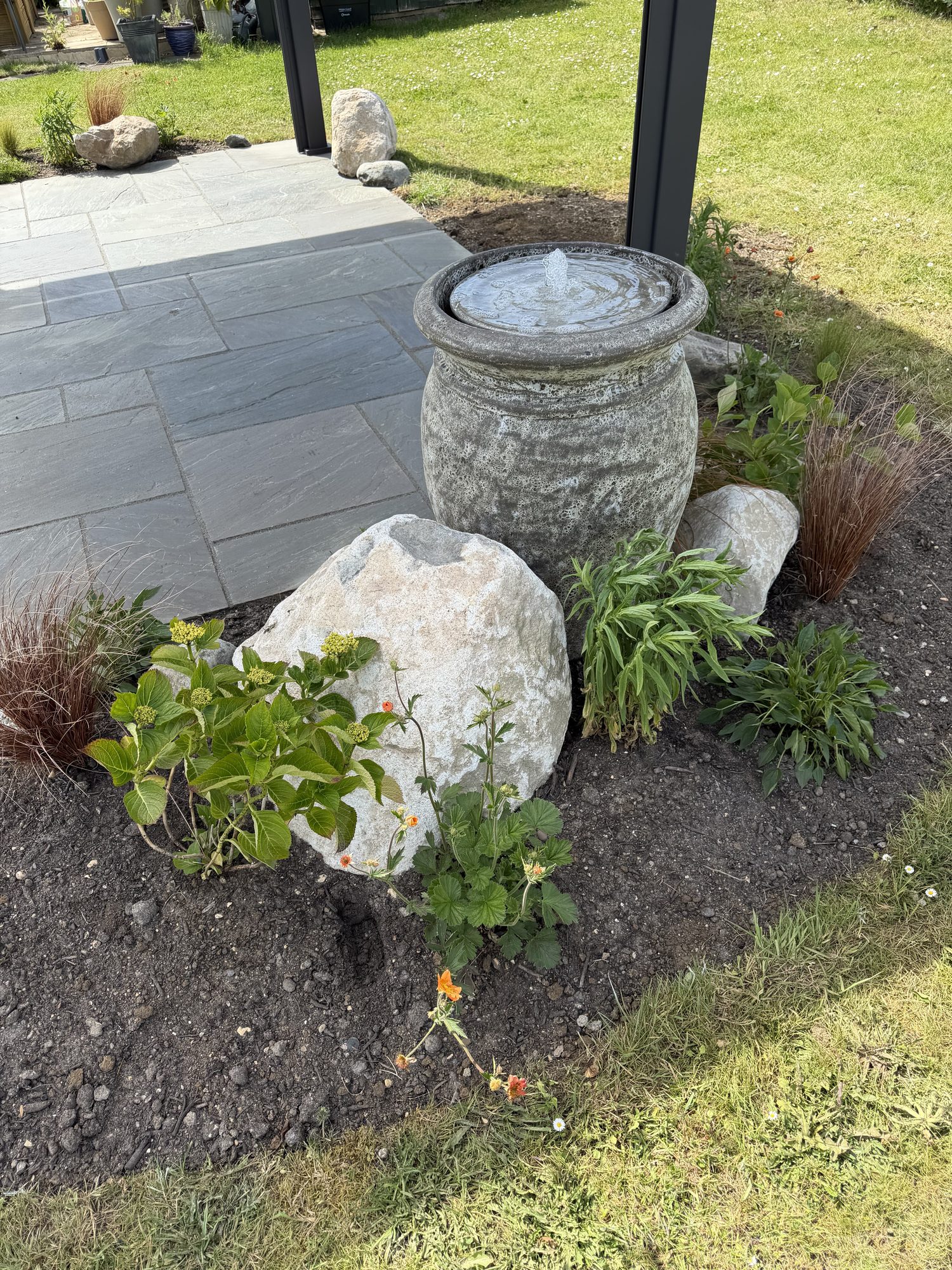 Stone urn water feature with a boulder and ornamental planting